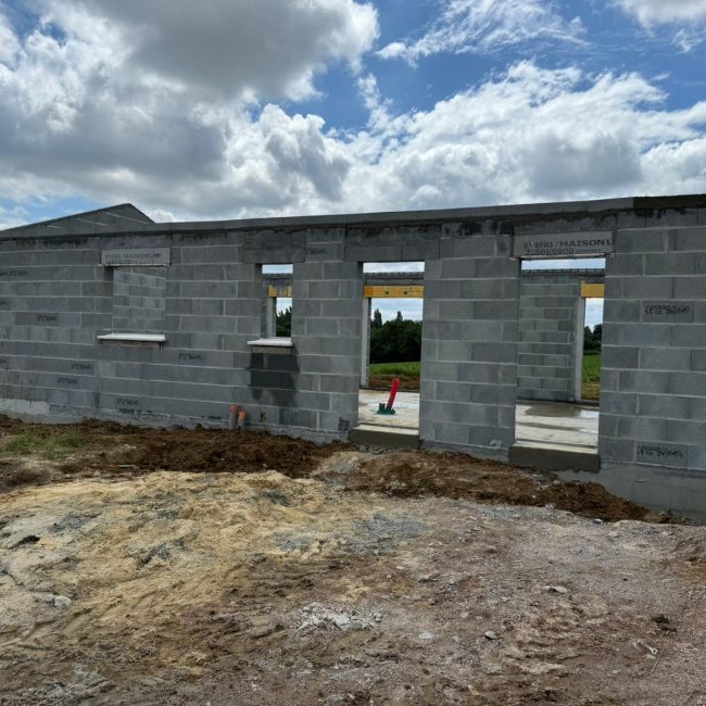 Construction d'une maison en parpaing, murs en parpaing avec ouvertures pour fenêtres et portes, ciel partiellement nuageux en arrière-plan