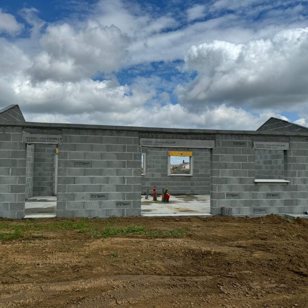 Construction d'une maison en parpaing, murs en parpaing avec ouvertures pour fenêtres et portes, ciel partiellement nuageux en arrière-plan